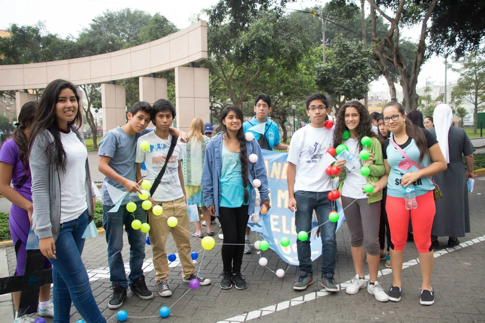 Grupo de jóvenes con estandarte y guirnaldas de globos frente a un arco